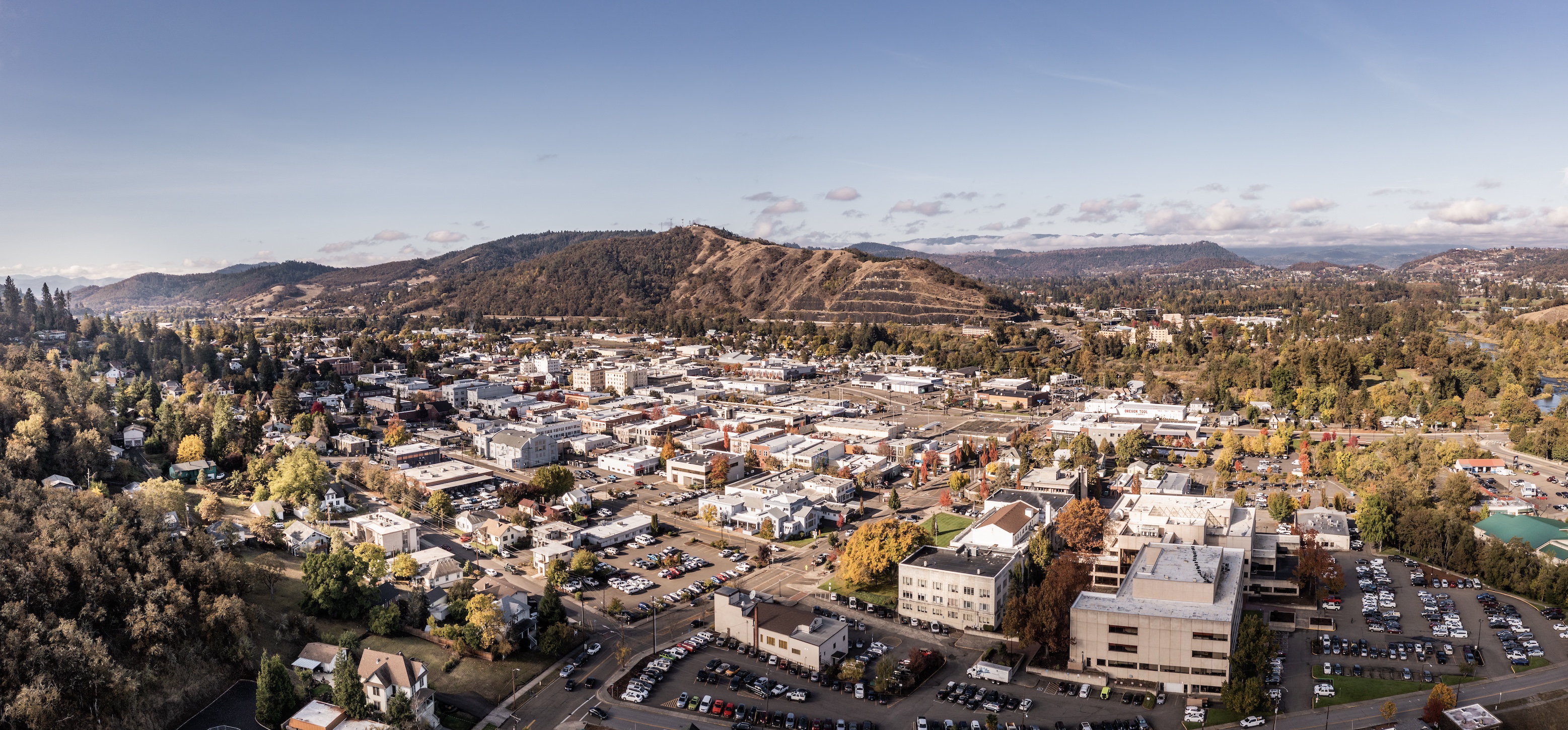 Aerial view of Roseburg, Oregon at golden hour, looking across downtown toward the surrounding mountains of Douglas County.